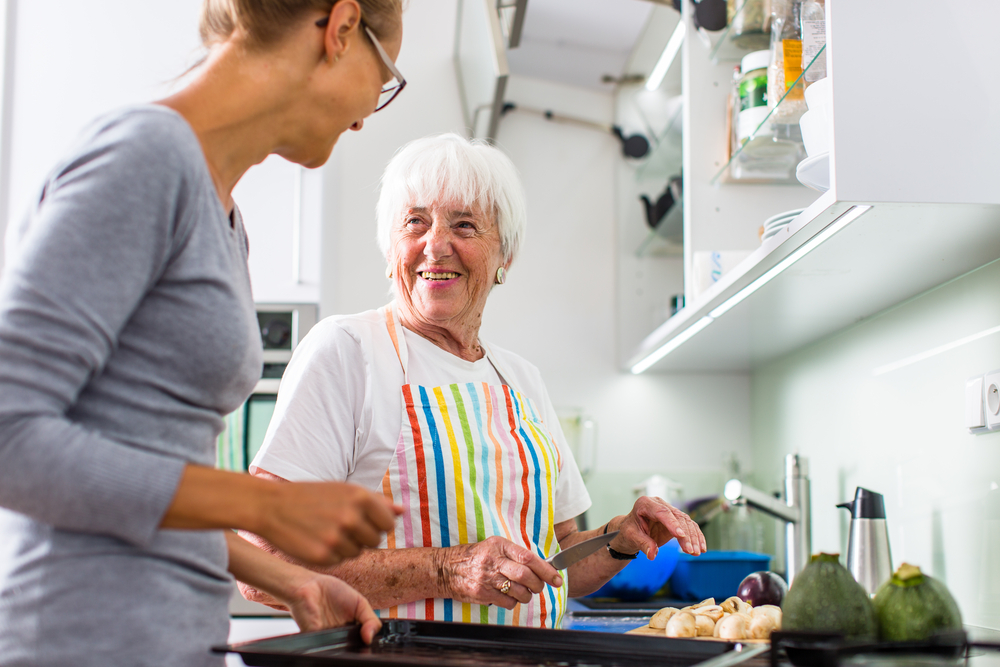 Els samen met jongere vrouw in de keuken in kleurrijk kookschort
